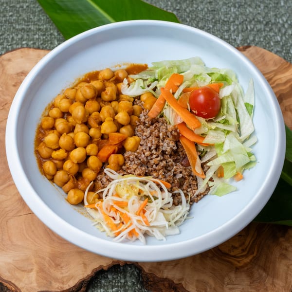 A Haitian dish with chickpeas, rice, shredded cabbage, carrots, lettuce, and a cherry tomato.