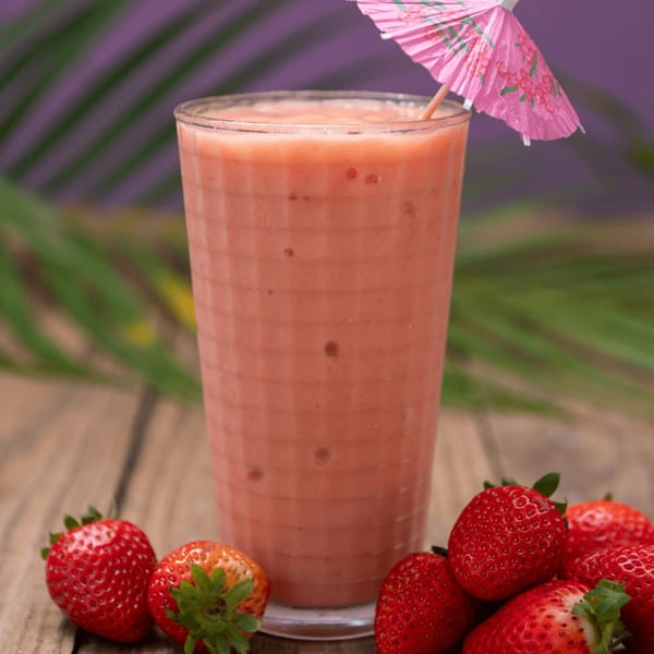 A strawberry smoothie with a pink umbrella and fresh strawberries on a wooden table.