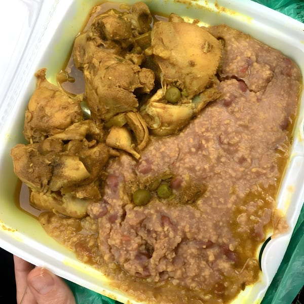 Haitian stewed chicken with a side of mashed beans and green peas in a white takeout container.