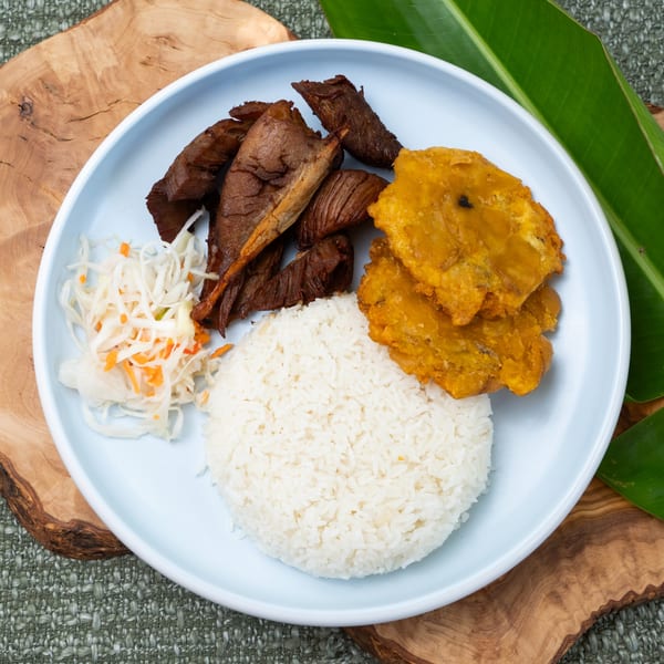 Haitian meal with fried plantains, white rice, pikliz, and dark meat on a light blue plate.