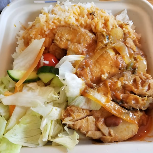 Haitian chicken in sauce with rice and a side salad in a takeout container.