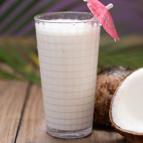 A refreshing coconut drink with a pink umbrella, next to a whole and a halved coconut.
