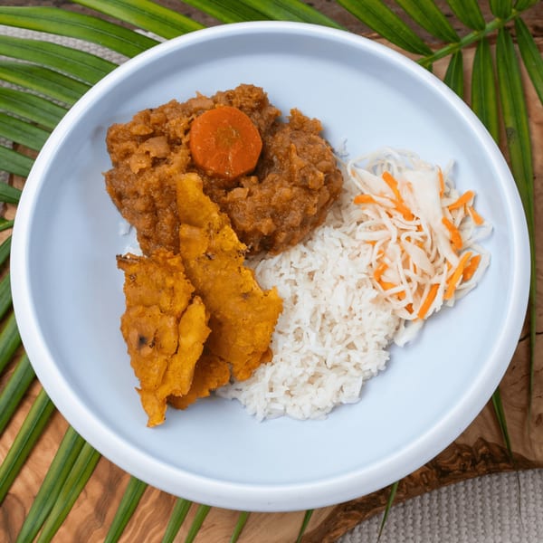 Haitian dish with rice, brown stew, fried plantains, and pikliz on a light blue plate.