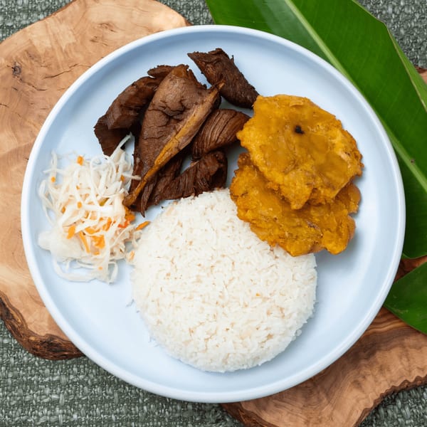 Haitian griot with white rice, fried plantains, and pikliz on a light blue plate.