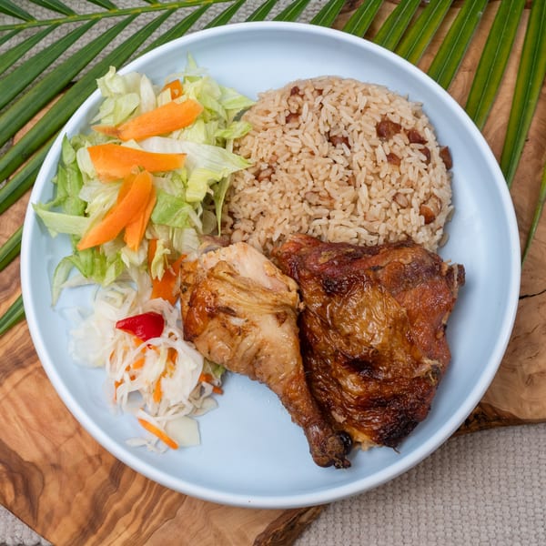 Haitian griot with rice and beans, pikliz, and fresh salad on a light blue plate.
