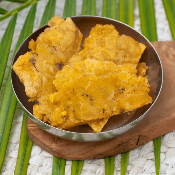 A metal bowl filled with golden-brown Haitian fried plantains, or tostones, on a wooden board.