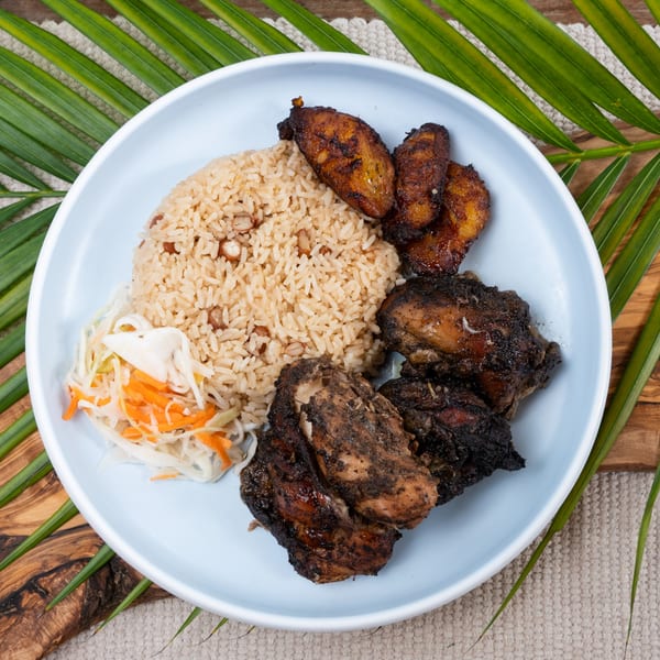 Haitian griot with rice and beans, fried plantains, and pikliz on a light blue plate.
