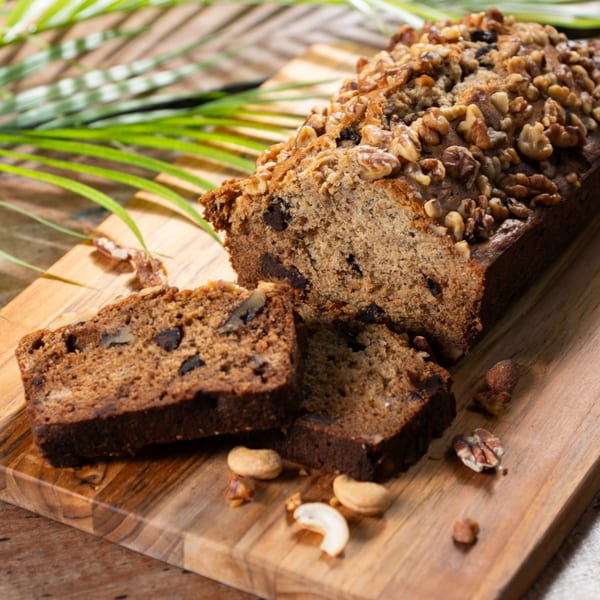 Haitian banana bread loaf with walnuts and chocolate chips, two slices cut, on a wooden board.