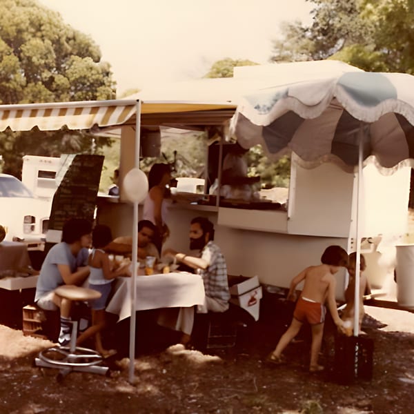 People gathered around a food stand with striped awnings, enjoying Haitian food outdoors.