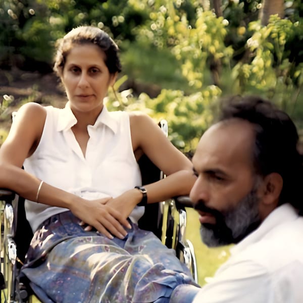 A woman in a wheelchair and a man in a white shirt in a garden setting.