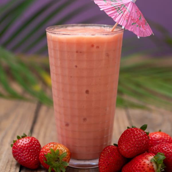 A Haitian strawberry smoothie with a pink umbrella and fresh strawberries on a wooden table.