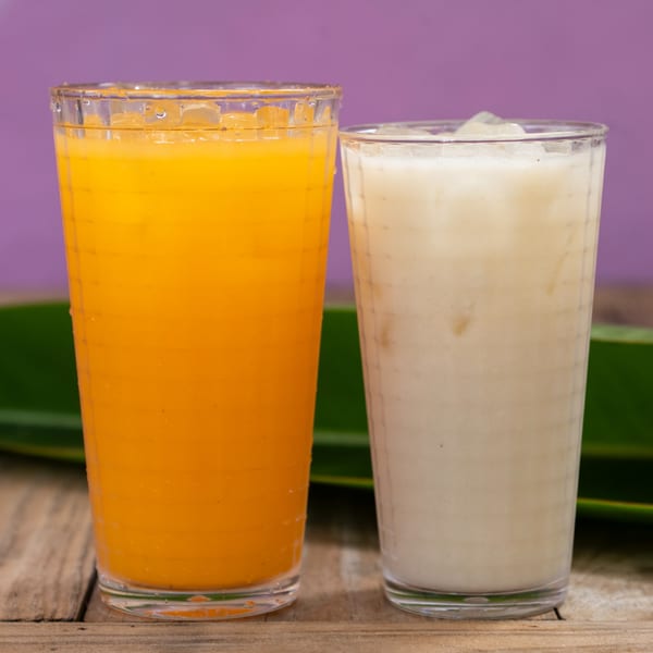 Two tall glasses, one with orange juice and one with a creamy white drink, on a wooden table.