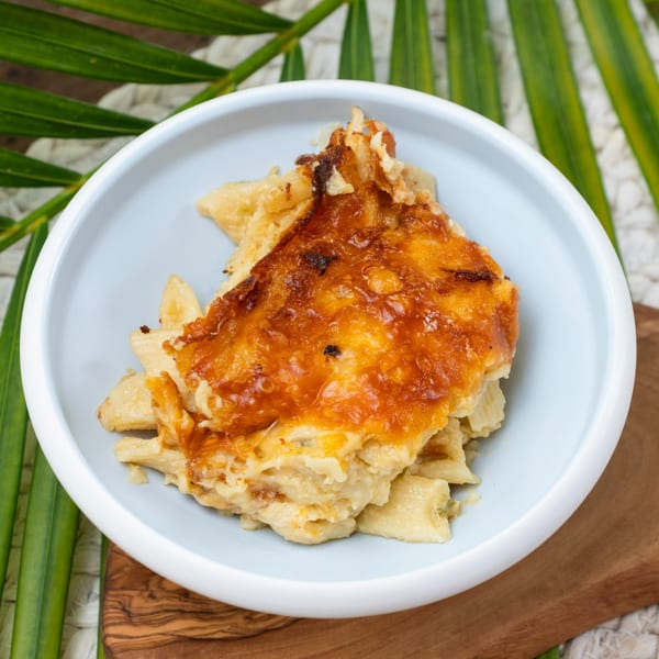 Haitian macaroni gratin, a baked pasta dish with a golden-brown cheesy crust, in a light blue bowl.