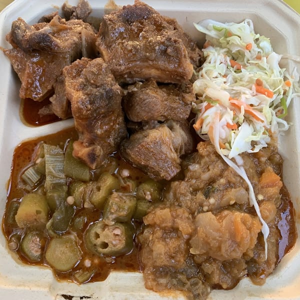 Haitian stewed beef with okra, a vegetable medley, and coleslaw in a takeout container.