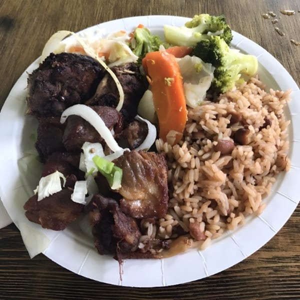 A Haitian dish with dark meat, rice and beans, and steamed vegetables on a white plate.