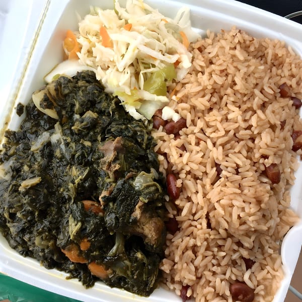 Haitian griot with rice and beans, stewed greens, and pikliz in a white takeout container.