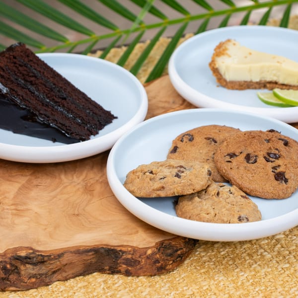 Chocolate cake, key lime pie, and chocolate chip cookies on light blue plates, on a wooden board.